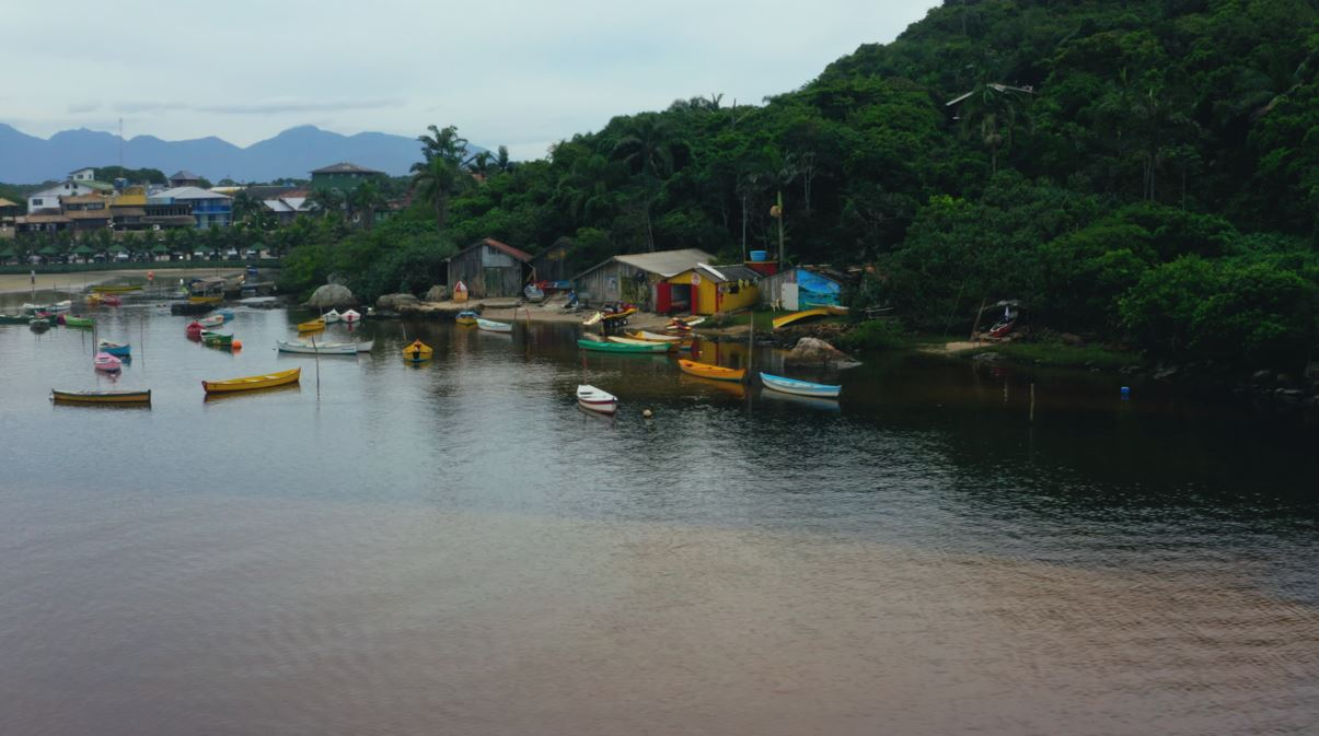 Imagem mostra um rio e casas de uma comunidade riberinha. Há algumas pequenas embarcações ali também,