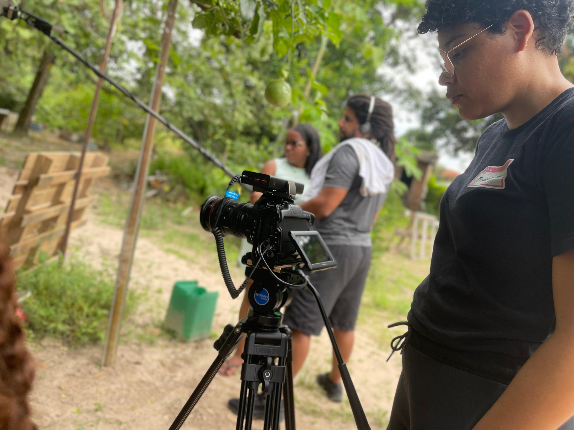 Uma equipe de filmagem trabalha em meio a um lugar árido, mas com vegetação com folhas verdes.