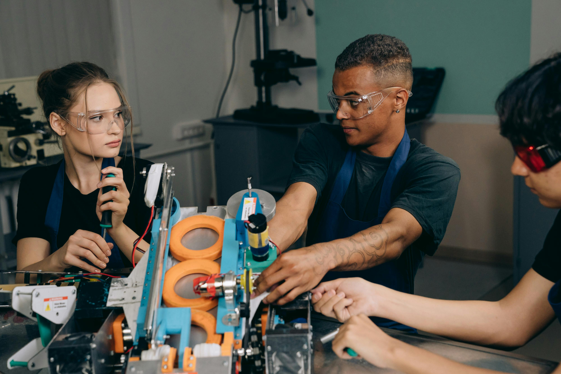 A imagem mostra três jovens em uma aula de robótica