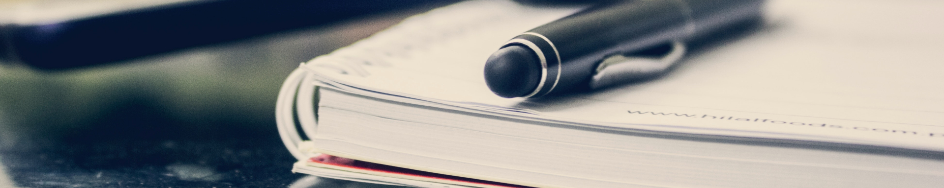 Uma caneta preta está apoiada em cima de um caderno ou livro branco