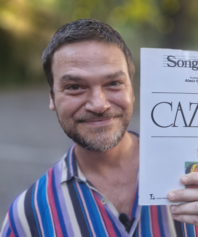 A imagem mostra o ator Emílio Dantas segurando o songbook do cantor Cazuza