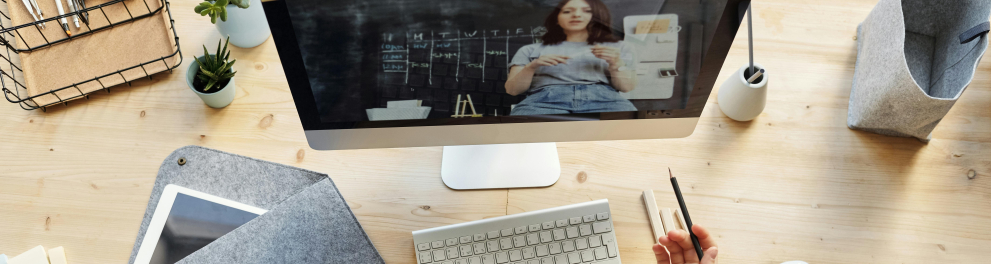 Mesa com teclado, um bloco com folhas brancas sobre os quais aparecem dois braços. Uma das mãos segura um lápis.