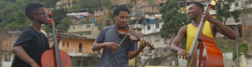 Três jovens tocam violino (o do meio) e violoncelos (os das pontas). Ao fundo, uma favela.