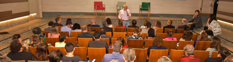 Plateia assiste a um homem de pé discursar em um auditório.