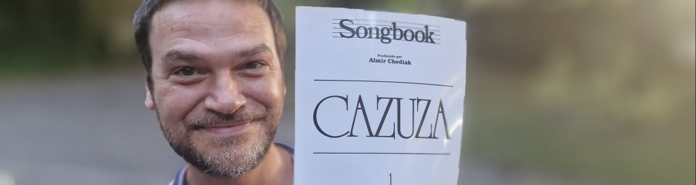 A imagem mostra o ator Emílio Dantas segurando o songbook do cantor Cazuza