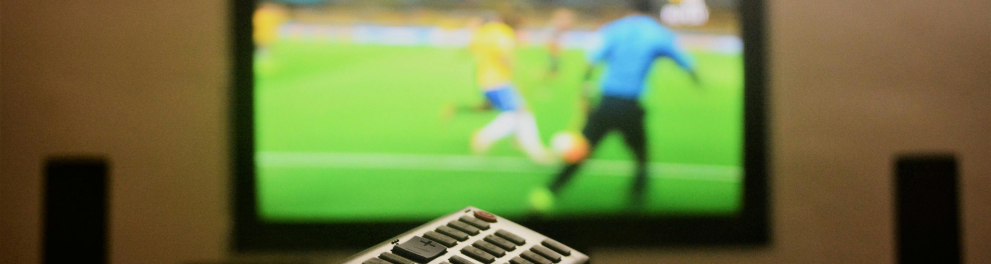 A imagem mostra uma televisão ligada na transmissão de uma partida de futebol 