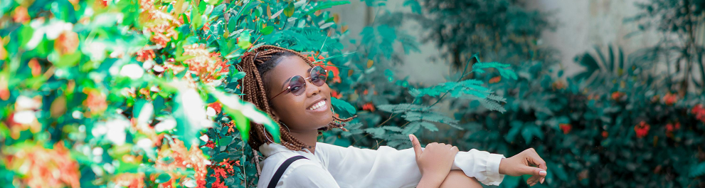 A imagem mostra uma jovem negra sentada em um gramado e posando para a foto