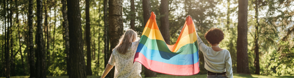 A imagem mostra duas mulheres segurando uma bandeira símbolo do movimento LGBTQIAPN+.