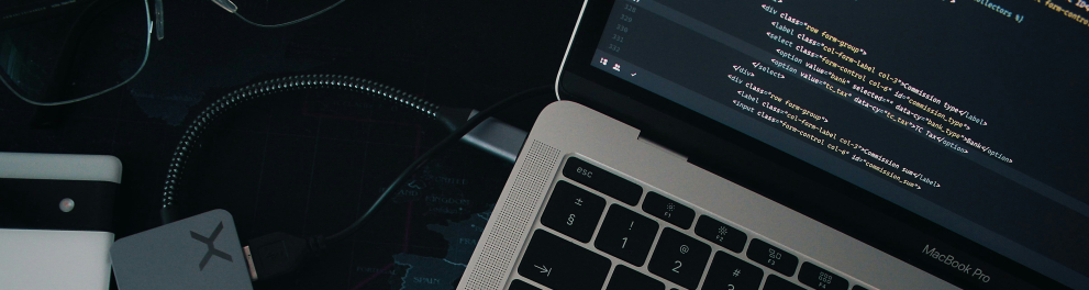 Um notebook visto parcialmente, aberto e exibindo uma tela com código de programação. O teclado preto com teclas iluminadas está em destaque. Ao lado do notebook, há um adaptador USB-C cinza conectado por um cabo. Também é possível ver um par de óculos, um caderno branco e um mapa-múndi estilizado como superfície da mesa. A iluminação é suave, sugerindo um ambiente de trabalho moderno e tecnológico.