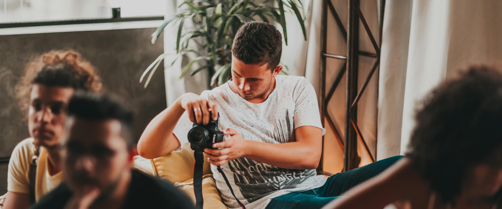 A imagem mostra um jovem tirando fotos com o auxílio de uma câmera fotográfica profissional durante um evento