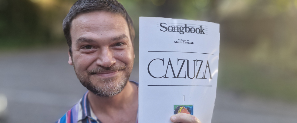 A imagem mostra o ator Emílio Dantas segurando o songbook do cantor Cazuza