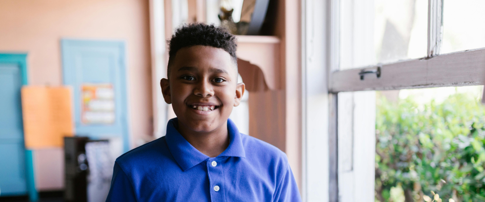A imagem mostra um menino com um livro aberto em mãos e sorrindo para a foto
