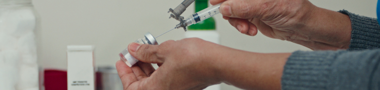 A imagem mostra uma pessoa aspirando uma vacina de um ampola para uma seringa