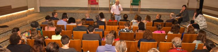 Plateia assiste a um homem de pé discursar em um auditório.