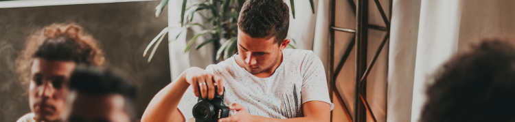 A imagem mostra um jovem tirando fotos com o auxílio de uma câmera fotográfica profissional durante um evento